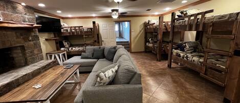 A cozy living room with a stone fireplace, a gray sectional sofa, and wooden bunk beds.