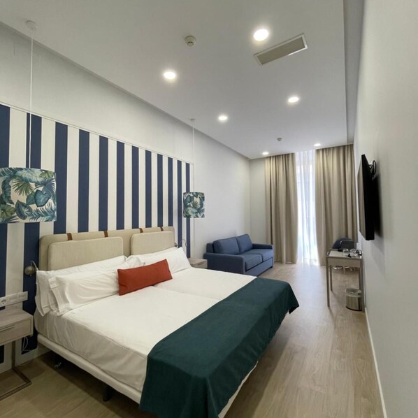Quarto de hotel com uma cama, um sofá, uma televisão e uma mesa com uma cadeira.