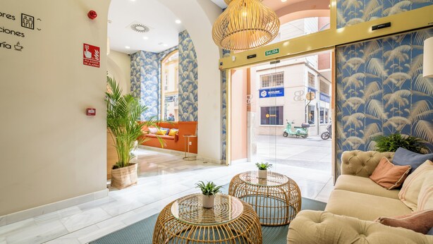 Un vestíbulo de hotel con una recepción, un sofá y un ventanal con vistas a la calle.