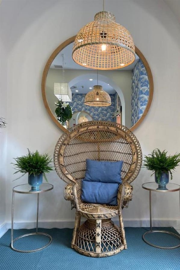 A wicker chair with a blue cushion in a room with a blue floor, a large mirror, and two potted plants. - Soho Boutique Urban (Málaga)