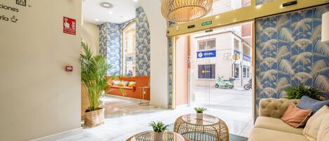 Um saguão de hotel com uma mesa de recepção, um sofá e uma grande janela com vista para a rua.