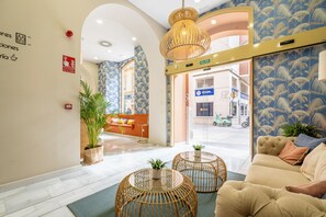 Un vestíbulo de hotel con una recepción, un sofá y un ventanal con vistas a la calle.