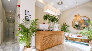 Un área de recepción con mostrador de madera, plantas en macetas y un espejo en la pared.