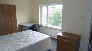 A bedroom with a bed, a desk, a chair, a wardrobe, and a window with a view of buildings and trees. - Luxurious Relaxing Room (Salford)