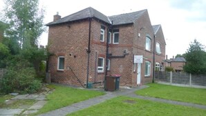 A two-story brick building with a sign indicating a business on the ground floor. - Luxurious Relaxing Room (Salford)