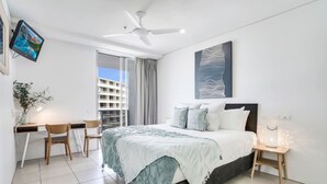 A modern hotel room with a bed, desk, chairs, a ceiling fan, a TV, and a view of a building through the window. - Studio Stay near Marina with Pool, Gym and Sauna (Cairns City)