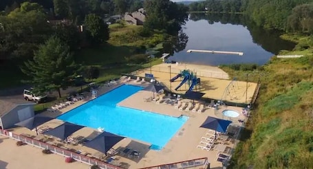 A swimming pool with a slide, surrounded by lounge chairs and a small deck area.