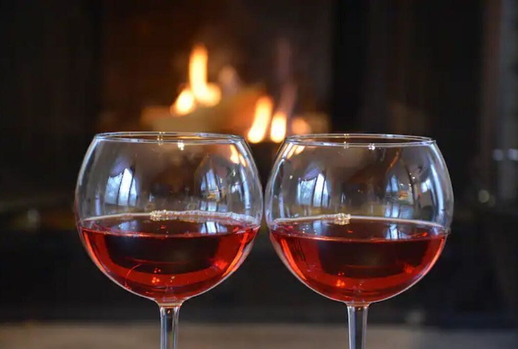 Zwei Weingläser mit Rotwein vor einem Kamin.