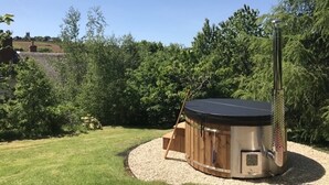 Un jacuzzi con cubierta de madera y calentador metálico, rodeado de grava y vegetación.