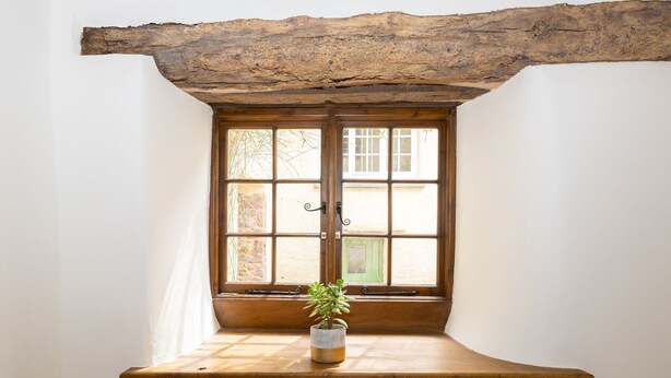 Una ventana con marco de madera y una planta sobre un repisa de madera.