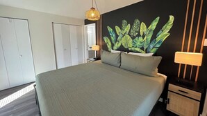 A modern bedroom with a large bed, a wall-mounted plant, a bedside table with a lamp, and a wardrobe.