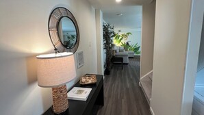 A hallway with a dark wood floor, a round mirror on the wall, a lamp, and a small table with decorative items.