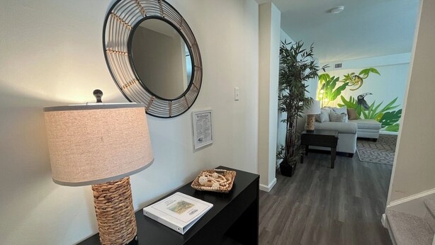 A modern living room with a round mirror, a lamp, a small table with a basket, and a sofa in the background.