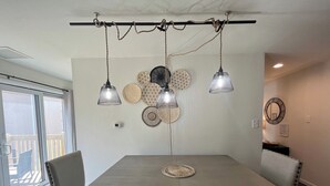A dining area with a rectangular table, four chairs, hanging pendant lights, and woven wall decorations.