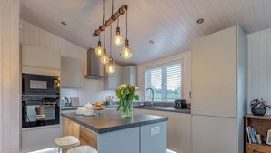 A modern kitchen with a central island, built-in appliances, and a window with blinds. - 2 bedroom accommodation in Willington, near Derby (Willington, near Derby)