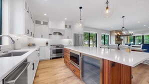 A modern kitchen with white cabinetry, stainless steel appliances, and a large island. - ExpERIEnce South Haven | Beach Farmhouse Steps to South Beach and Lake Michigan (South Haven)
