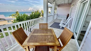 Ein Holztisch und -stühle auf einem überdachten Balkon mit Blick auf das Meer und angrenzende Häuser.
