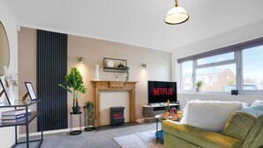 A modern living room with a fireplace, a television displaying 'NETFLIX', and a sofa. - Stylish House • Sleeps 6 • Driveway Parking • Garden • Fast Wifi • Self-Check-In • Yoko Property (Coventry)