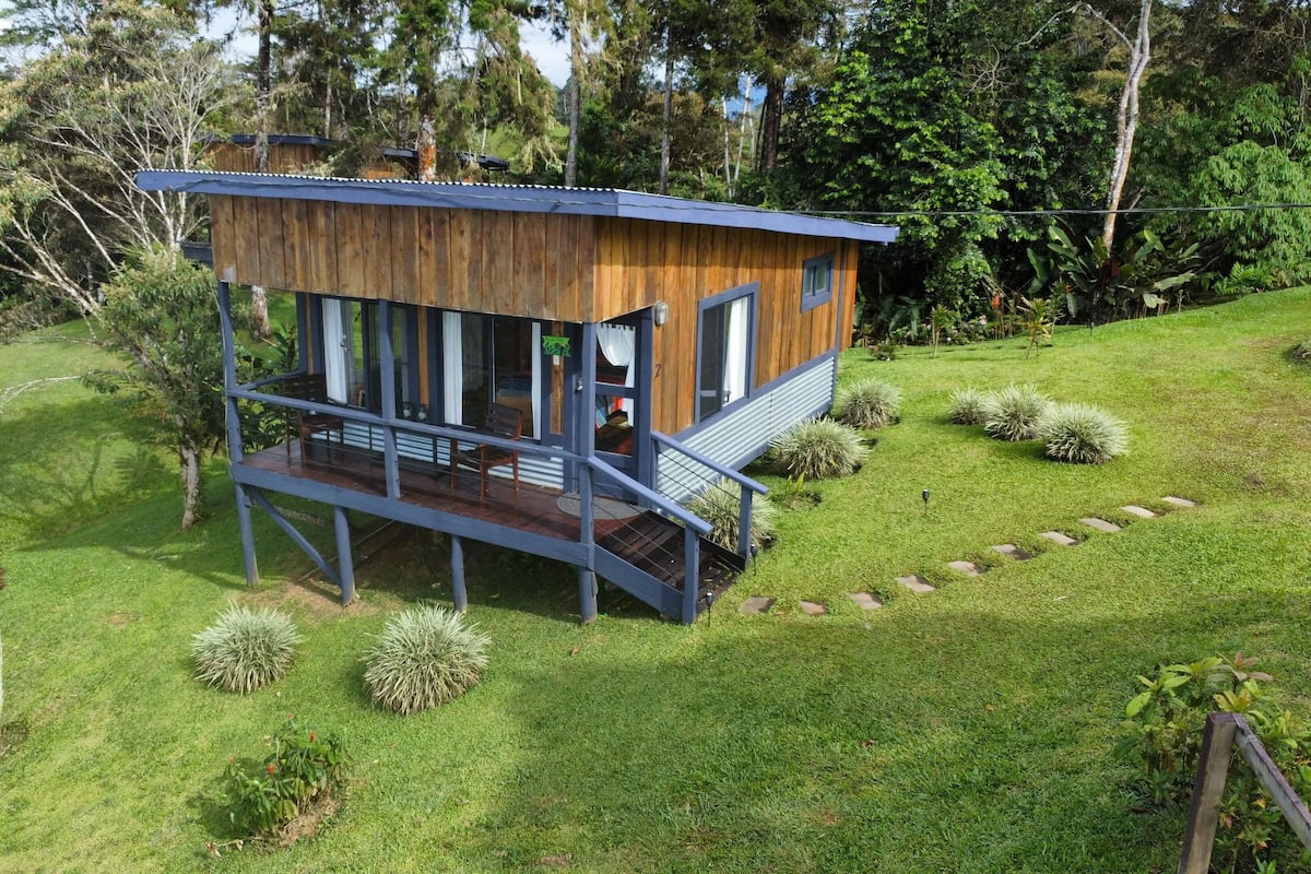 A wooden cabin with a balcony, surrounded by lush greenery and trees.