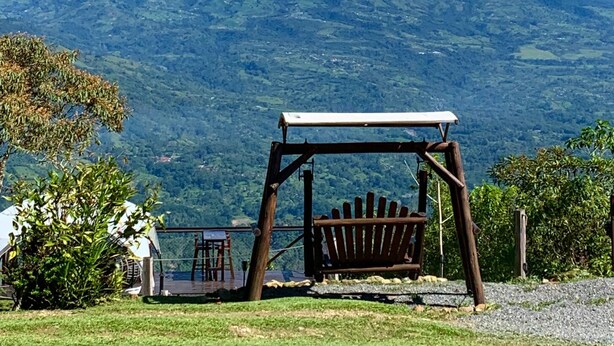 A wooden swing set with a bench, a small table, and chairs in a grassy area with a mountain view.