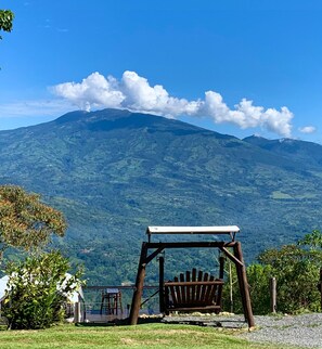 A wooden swing set with a bench, a small table, and chairs in a grassy area with a mountain view. - Reventazon River Mountain Lodge (Pavones)