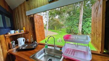 Una cocina de madera con un lavamanos de acero inoxidable, una tetera y un escurreplatos.