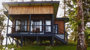 A two-story wooden cabin with a balcony, surrounded by greenery.