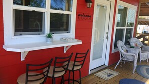 Une façade rouge avec une fenêtre blanche, une enseigne accueillante et une véranda dotée de fauteuils et d’une table en osier.