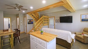 Une chambre à coucher avec un lit, un bureau en bois, une chaise, une commode, un escalier et un téléviseur fixé au mur.