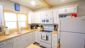 Une cuisine avec des meubles blancs, un four à micro-ondes, un four traditionnel, un évier et un réfrigérateur.