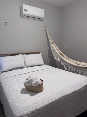 A bedroom with a bed, a hammock, and an air conditioning unit.