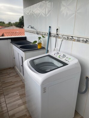 Une petite buanderie équipée d’un lave-linge à chargement frontal, d’un petit évier et d’une plante en pot.