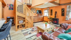 Un salon chaleureux avec un escalier en bois, une cheminée, un téléviseur et un coin repas comprenant des chaises et une table.