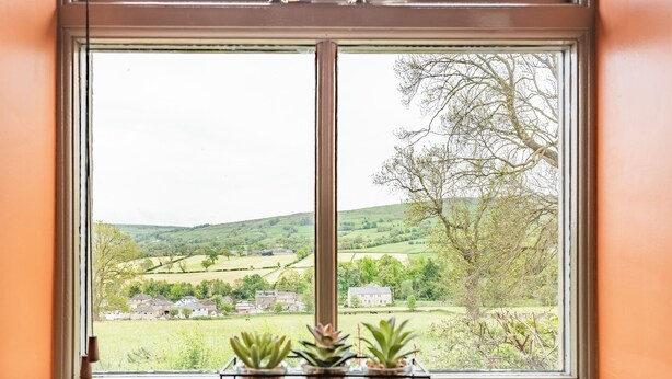 Une fenêtre donnant sur un paysage rural, avec des maisons et des arbres.