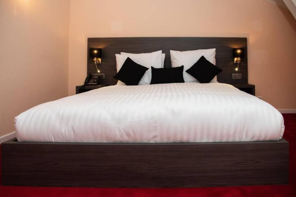 A neatly made bed with a dark headboard, white bedding, and black pillows. There are two bedside tables with lamps and a telephone on one side.