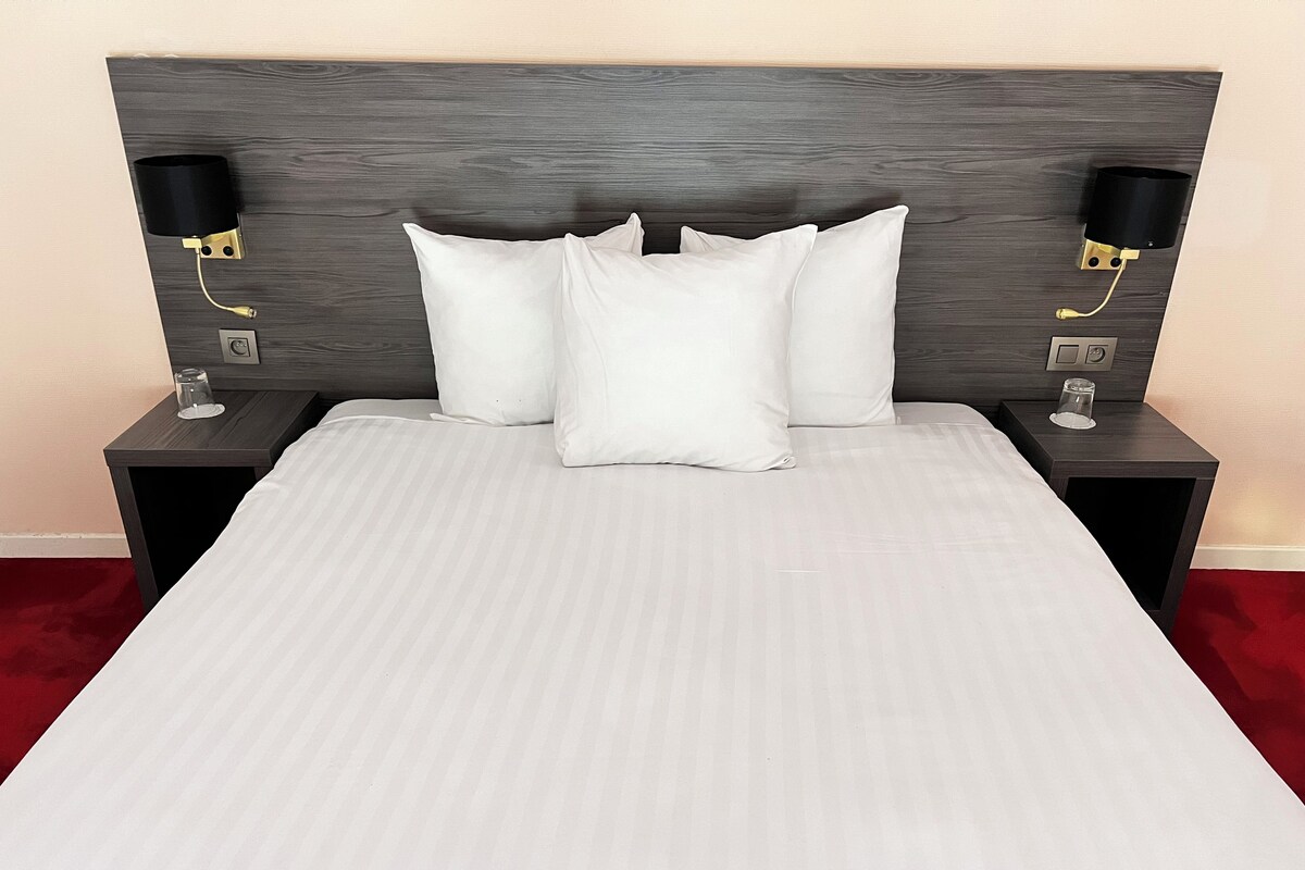 A bed with a grey headboard, two bedside lamps, and a glass on the nightstand.