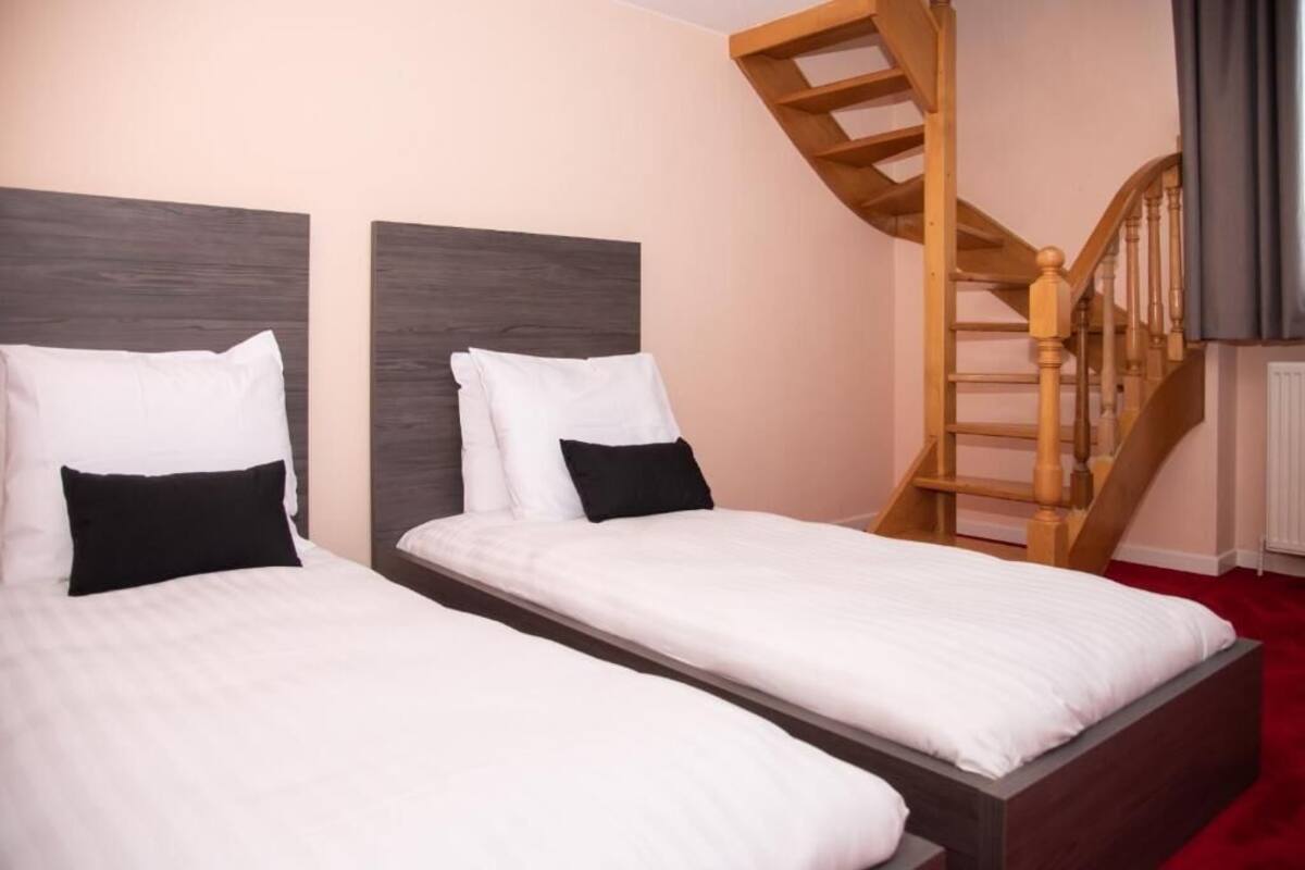 A hotel room with two beds, a wooden staircase, and a red carpet.