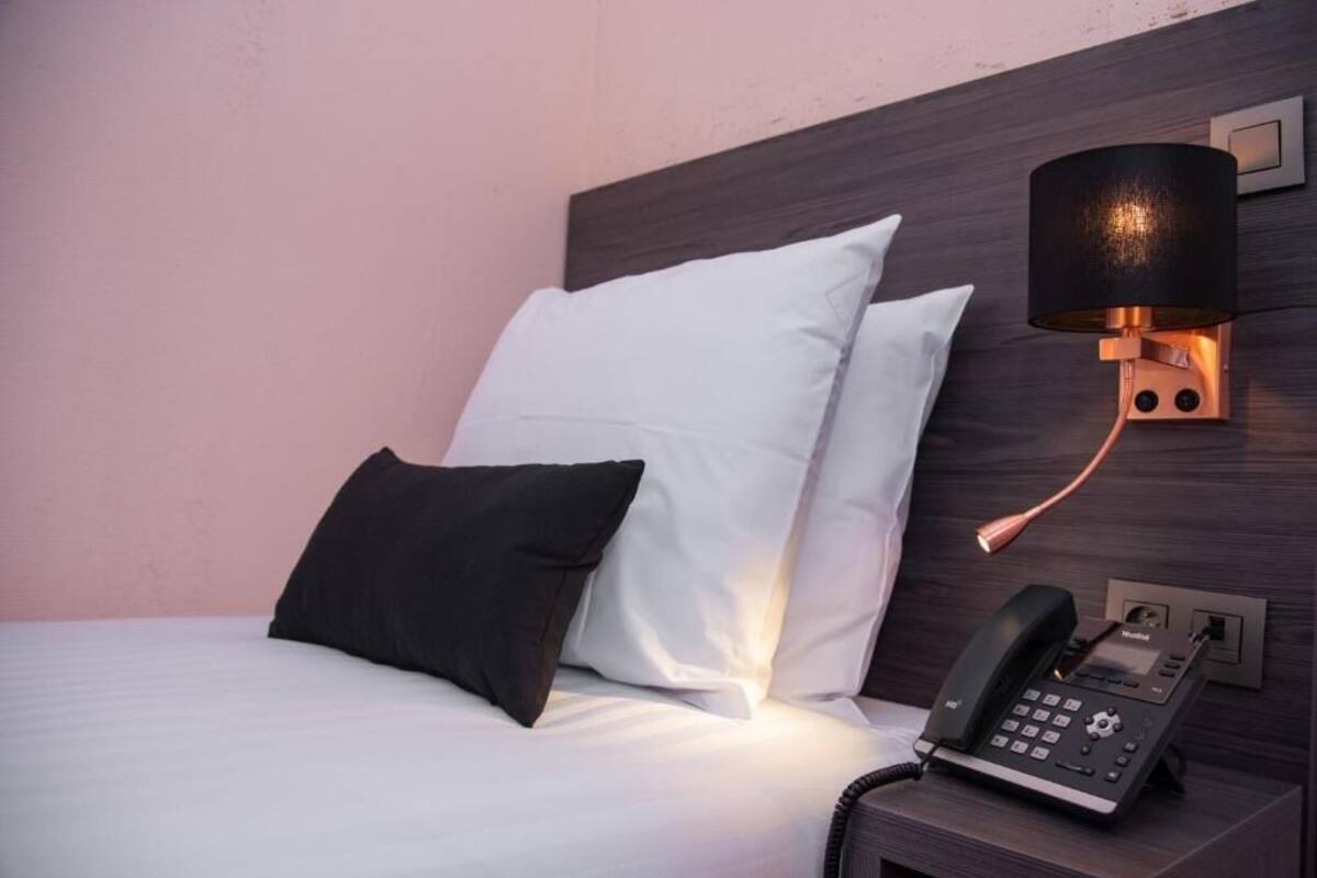 A hotel room with a bed, two pillows, a bedside lamp, and a telephone.