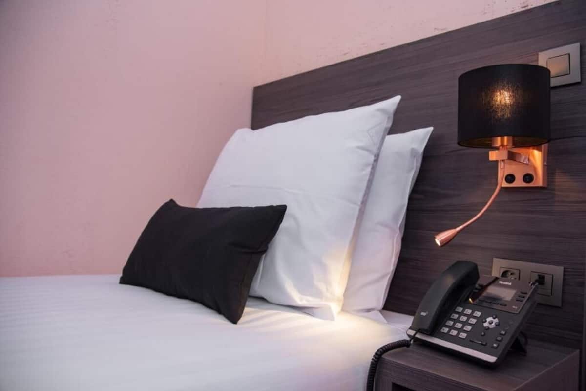 Ett hotellrum med en säng, två kuddar, en sänglampa och en telefon.