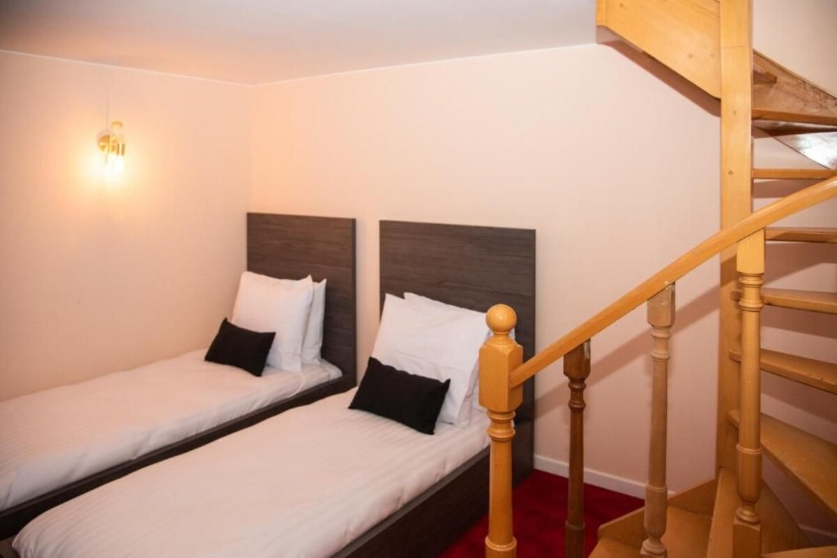 A bedroom with two single beds, a wooden staircase, and a wall-mounted light fixture.