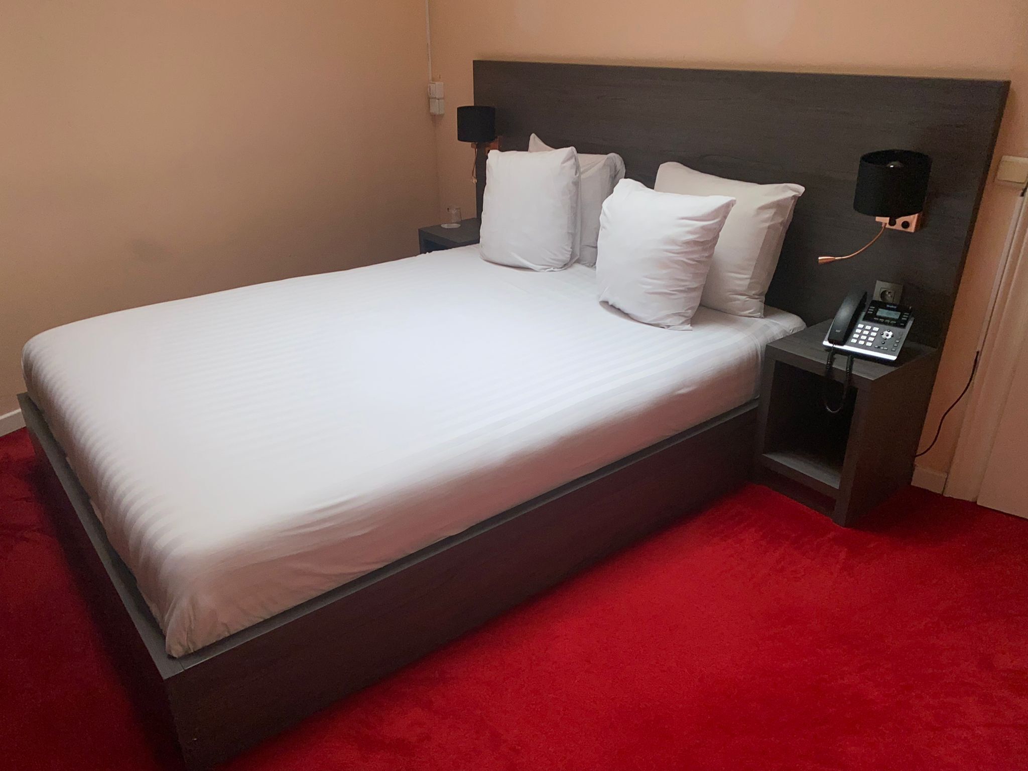 A single bed with white linens, a bedside telephone, and a nightstand with a lamp.