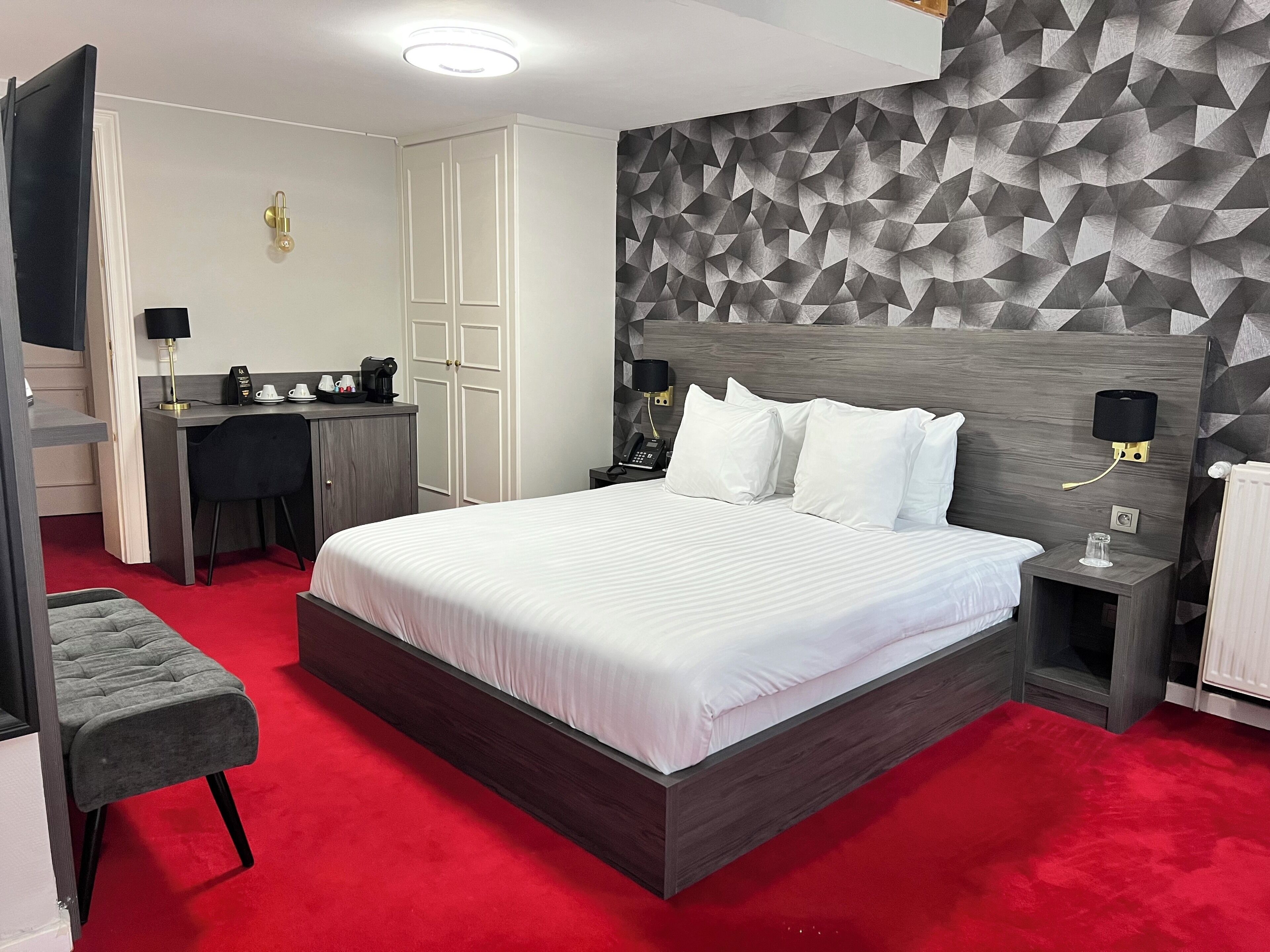 A modern hotel room with a large bed, a desk, and a wardrobe.