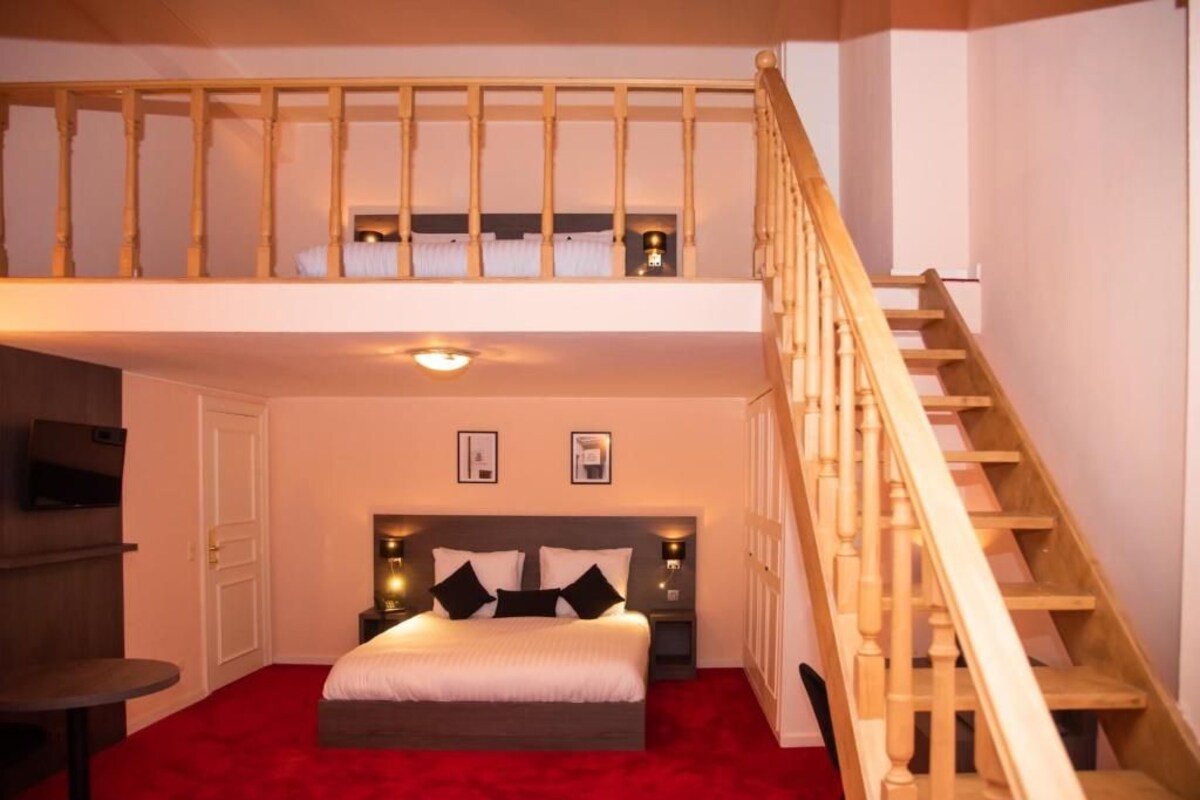 A bedroom with a bed, a small table, a TV, and a staircase.