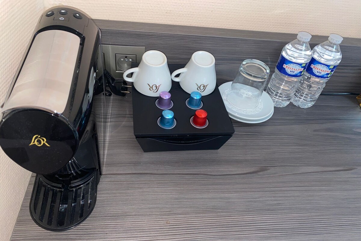 A coffee machine, two white cups, a glass, and two bottles of water on a wooden surface.