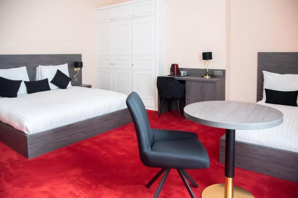 A hotel room with two beds, a desk, a chair, and a round table.