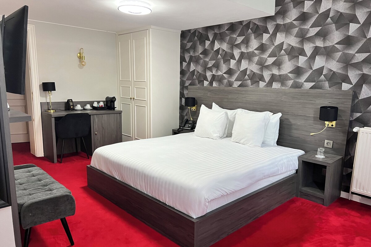 A modern hotel room with a large bed, a desk, and a wardrobe.