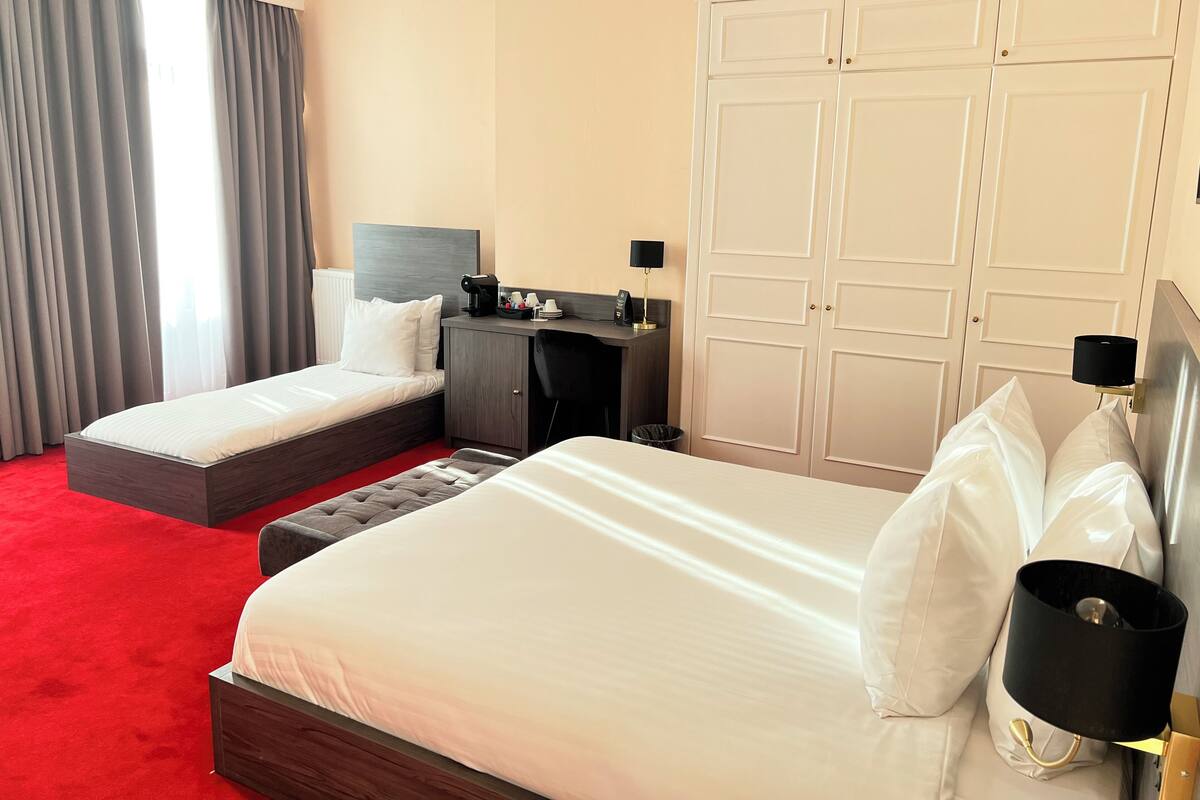A hotel room with two beds, a desk, a wardrobe, and a window with curtains.