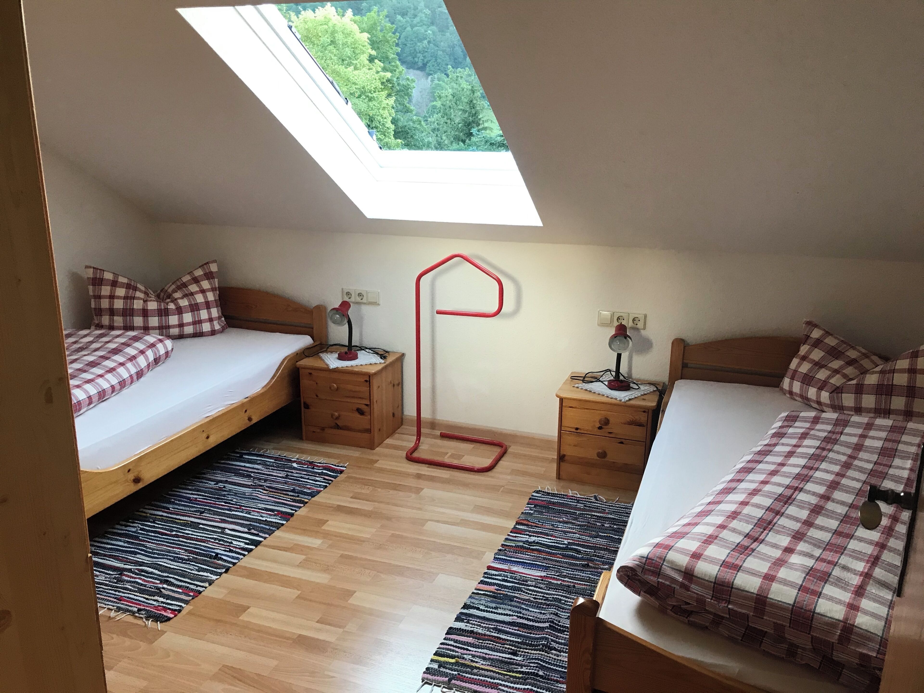Ein kleiner, gemütlicher Raum mit zwei Betten, jeweils mit karierter Bettdecke, Holzboden und einem Oberlicht.
