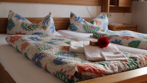 Een netjes opgemaakt bed met een bloemenprint deken, kussens met vergelijkbare motieven, en een rode roos op het bed.