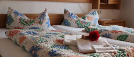 A neatly made bed with a floral-patterned bedspread, pillows with similar designs, and a red rose on the bed.